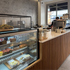 A cafe service counter with a glass cabinet next to it that displays assortment of cakes, breads and sandwiches.