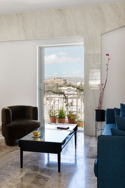 Modern living room with a view of the Acropolis, featuring a glass coffee table, a black armchair, and a blue sofa.