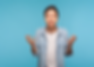 Man in a denim shirt gestures with open hands against a blue background, appearing surprised or questioning. He has short dark hair.