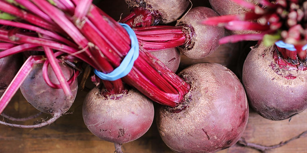 Bundled red beets with stalks and blue bands on a wooden surface, showcasing vivid red and purple hues.