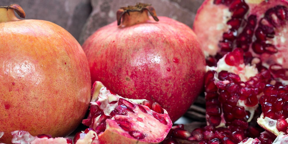 Close-up of two whole pomegranates and one halved, revealing red seeds. The background is blurred, highlighting the fruit's vibrant hues.