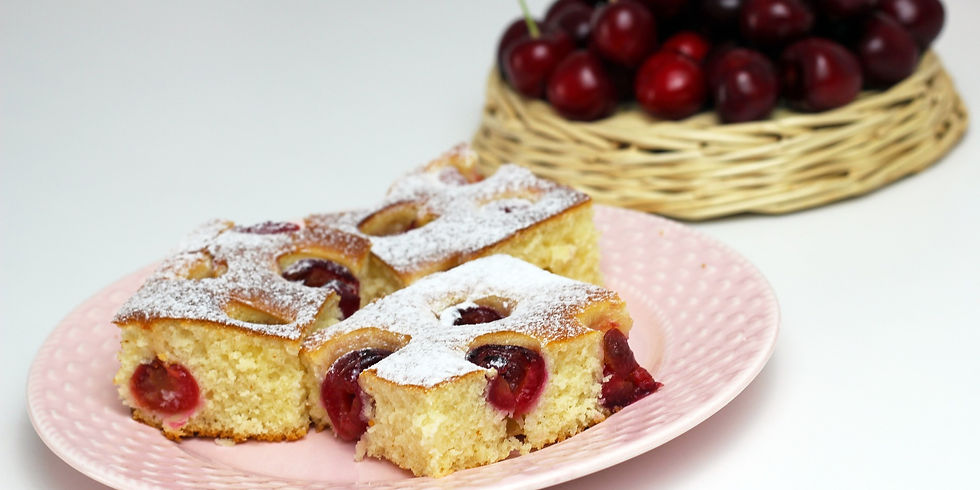 Three cherry cake slices with powdered sugar on a pink plate, next to a basket of fresh cherries. Bright and appetizing setting.