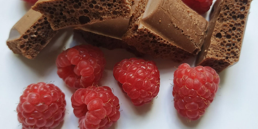 Raspberries and aerated chocolate pieces on a white surface. The vibrant red berries contrast with the brown, bubbly chocolate.