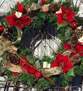 Festive wreath with red bows and pinecones on a rustic wooden fence. 