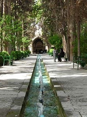 Garden with a long water channel, green benches, surrounded by trees.