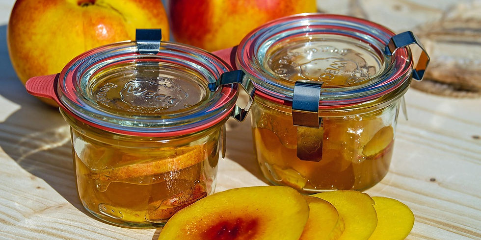 Jars of nectarine preserves on a wooden surface with fresh peaches and peach slices nearby. Jars have red and blue clips and lids.