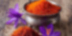 Silver bowl filled with vibrant saffron threads on rustic wooden surface, surrounded by blooming purple saffron flowers.