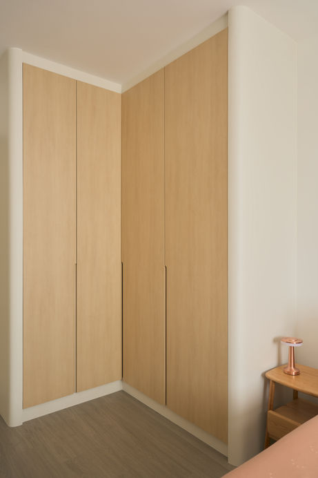 Built-in corner wardrobe with seamless wood laminate doors and rounded wall edges in soft neutral tones.