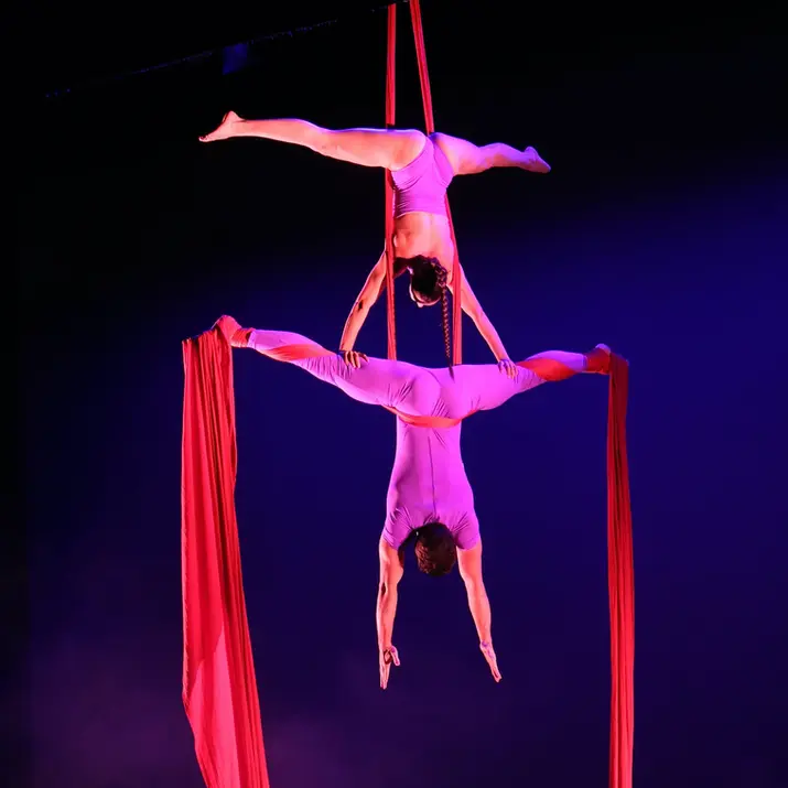 Handstand on red aerial silks duo on stage on a theatre. Both aerial acrobats are upsidedown.