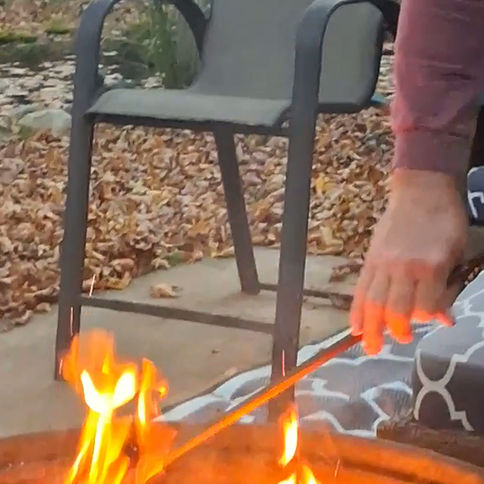 Person using a fire poker to adjust burning logs in an outdoor fire pit.