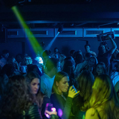 Foto einer Party im Raum Musicclub. Die Feiernden stehen, tanzen und trinken.