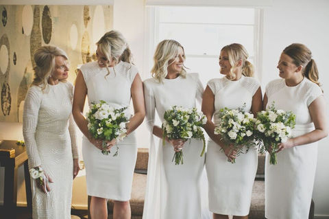 Mother of the bride wearing a wedding wrist corsage and standing with bride and bridesmaids holding classic white wedding florals