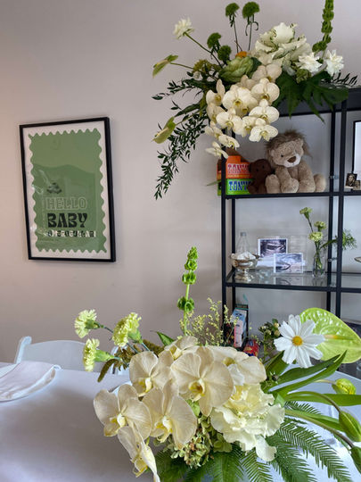 Flowers sitting on the shelf as well as on the table. lush orchids and mixed blooms.