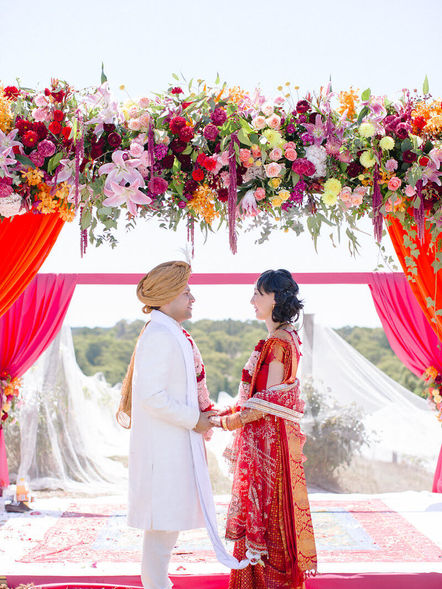 Bride and groom holding hands under mandap decorated in colourful wedding florals