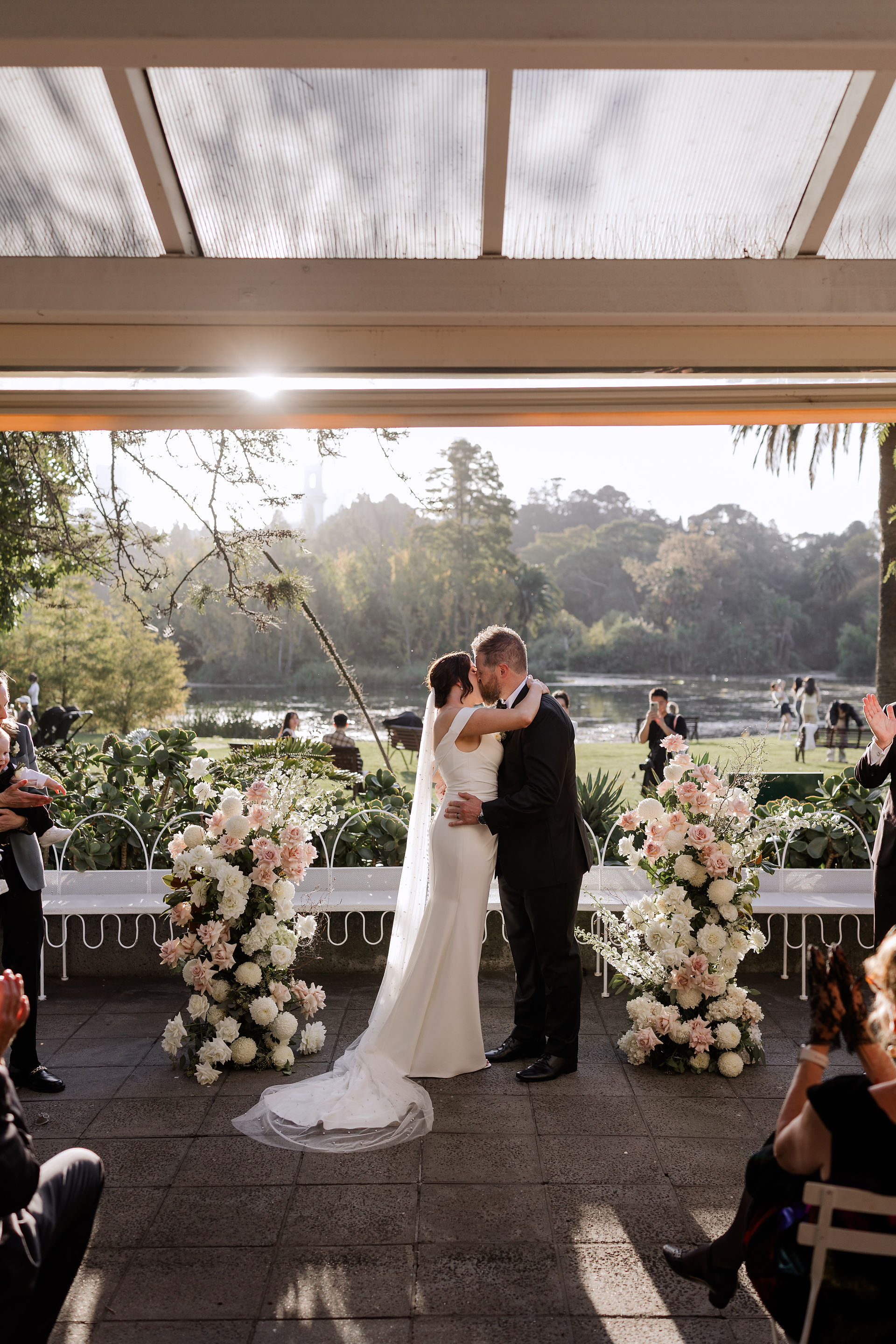 Bride and Groom kissing after saying I do on the terrace in the Botanical Gardens. Surrounded by fresh pink and white flowers