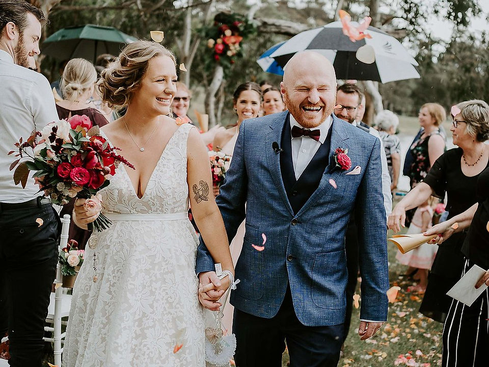 bride and groom smiling as they walk down the aisle hand in hand carrying a wedding bouquet
