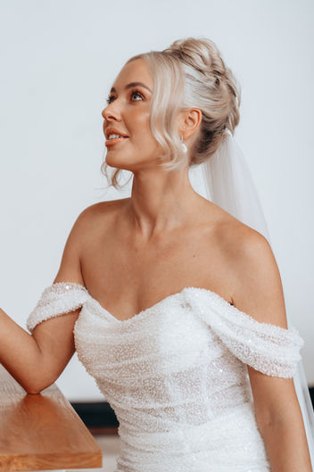 Mid length shot of blonde bride in wedding dress looking up into the distance on plain background. Makeup and Hair by Jessica Bailey
