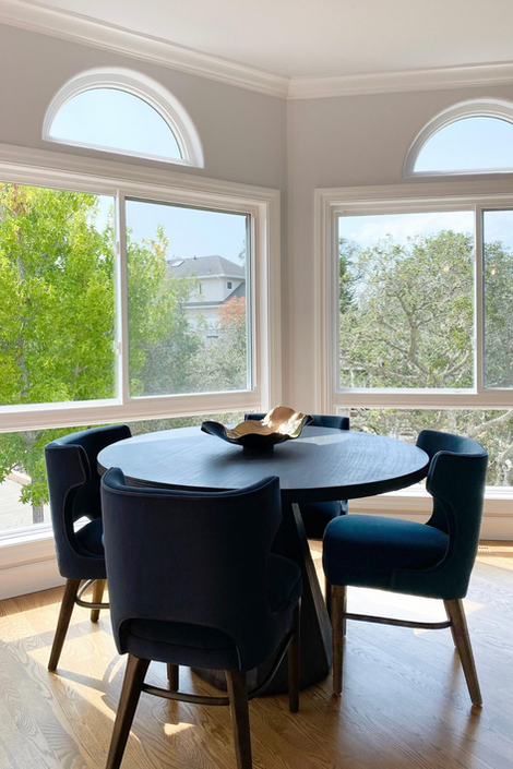 Dining area with round table, navy chairs, and bay windows with garden view