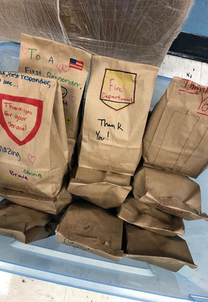A large bin holds more than a dozen lunch bags decorated by children with messages like "Thank you firefighters" and "Pay it Forward 9/11"