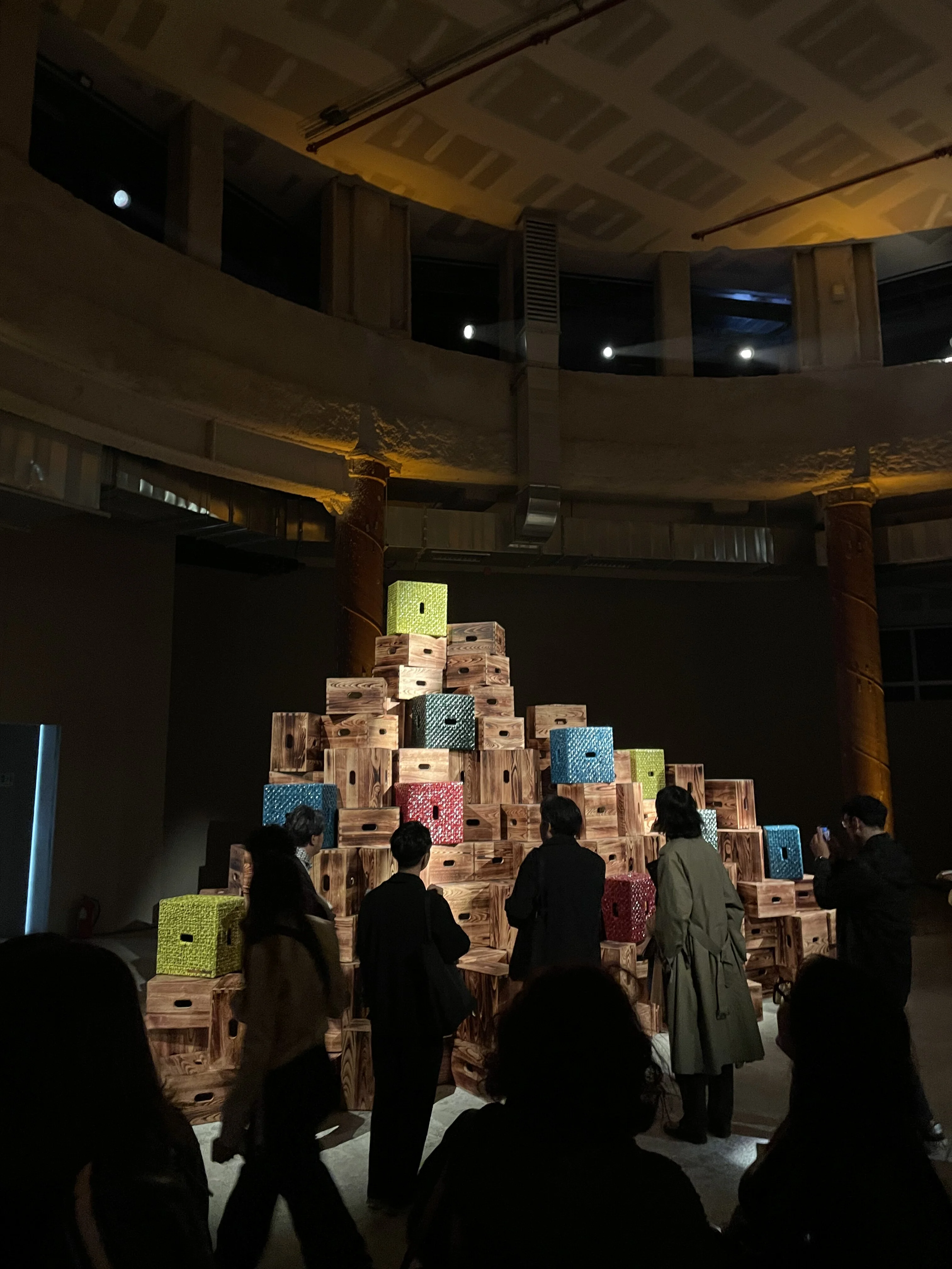 A creative display of colorful, patterned boxes stacked in a pyramid formation in a dimly lit exhibition space.