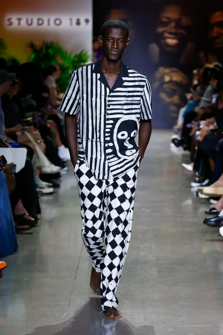 Runway model in a black and white striped shirt with matching checkered trousers, showcasing a bold, graphic fashion statement.