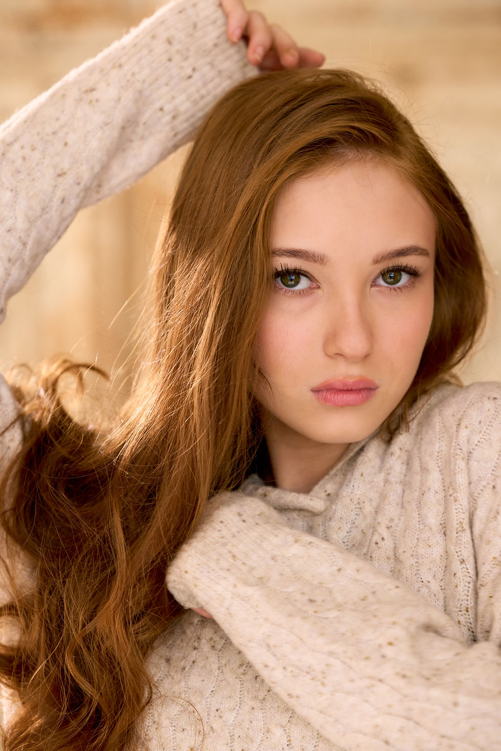 Caroline Elle Abrams from Stranger Things  poses with one arm raised, wearing a beige sweater. 