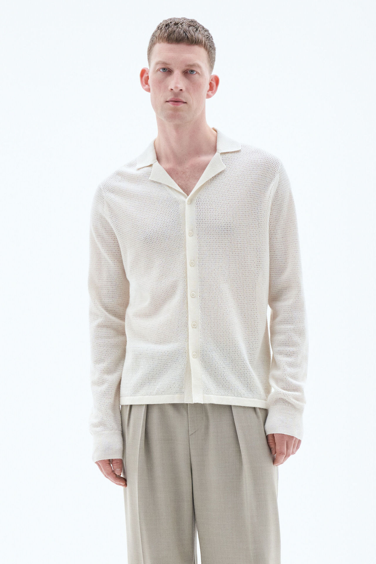 Male model in a casual beige knit polo shirt and matching trousers posing against a white background.
