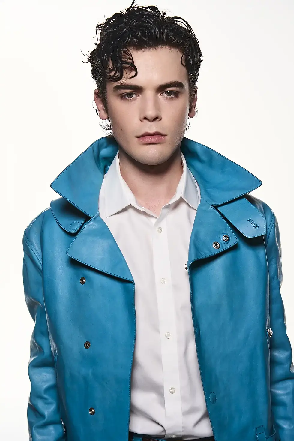 Duncan Joseph with curly dark hair in a bright blue jacket and white shirt, standing against a plain white background.