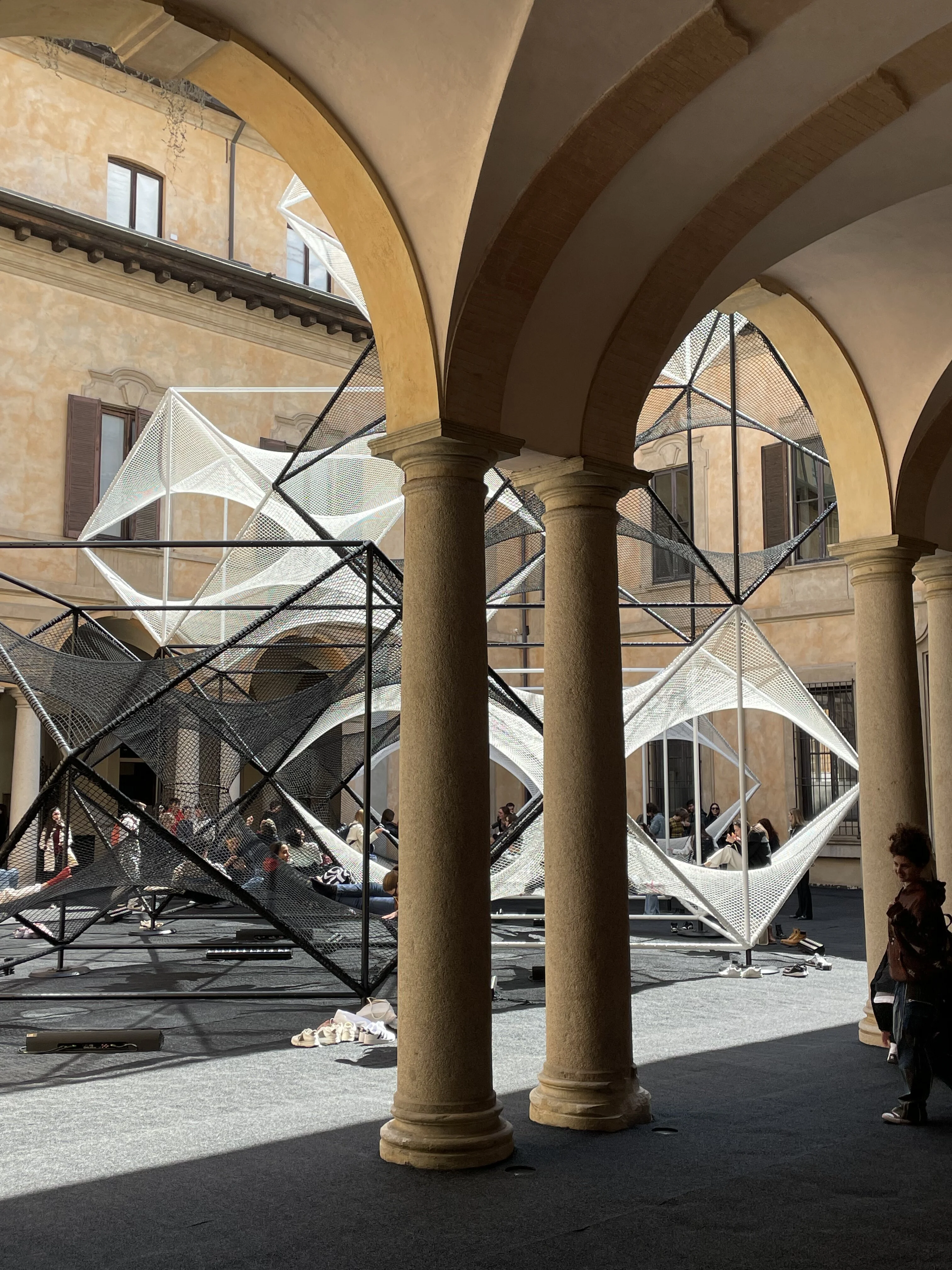 n intricate mesh installation at Milan Design Week, stretching across a courtyard with historical arches.