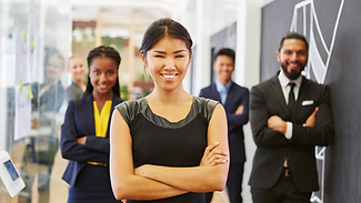 Young Professional Woman stnading in front of a group of diverse group of young professinals in a business lobby.