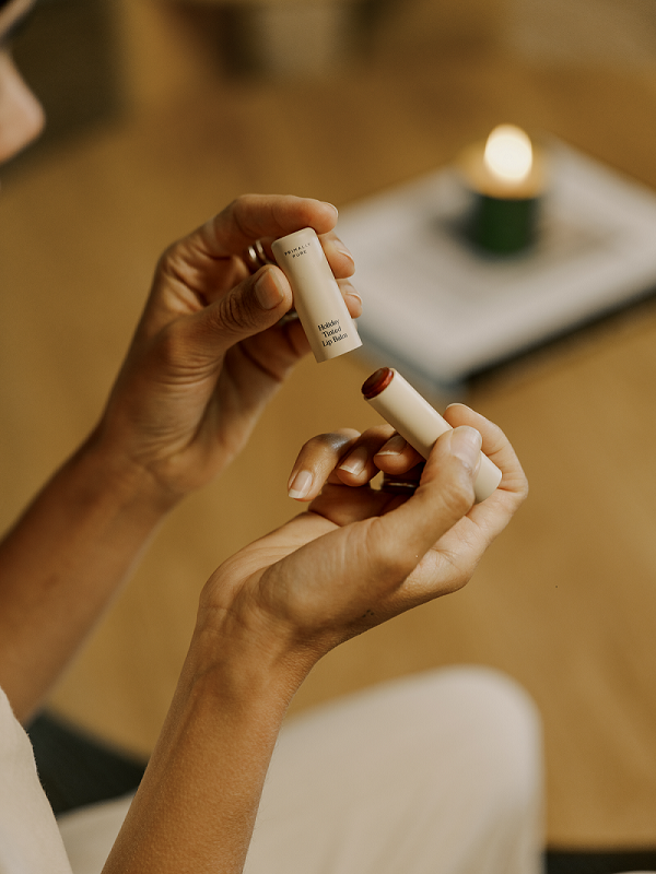 Hands opening Primally Pure tinted lip balm during a calming self-care moment at home.