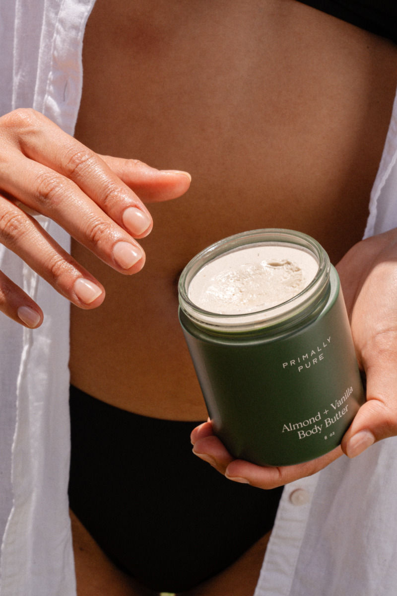 Person holding a jar of Primally Pure Almond + Vanilla Body Butter near their midsection.