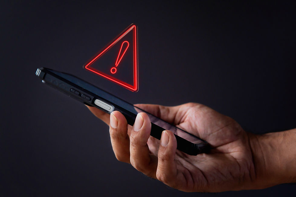 Hand holding a smartphone with a red warning triangle hologram above. Dark background; sense of alert or caution.