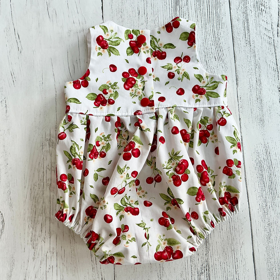 Thumbnail: Sleeveless baby romper in a cotton fabric featuring clusters of red cherries & green foliage on an off white background