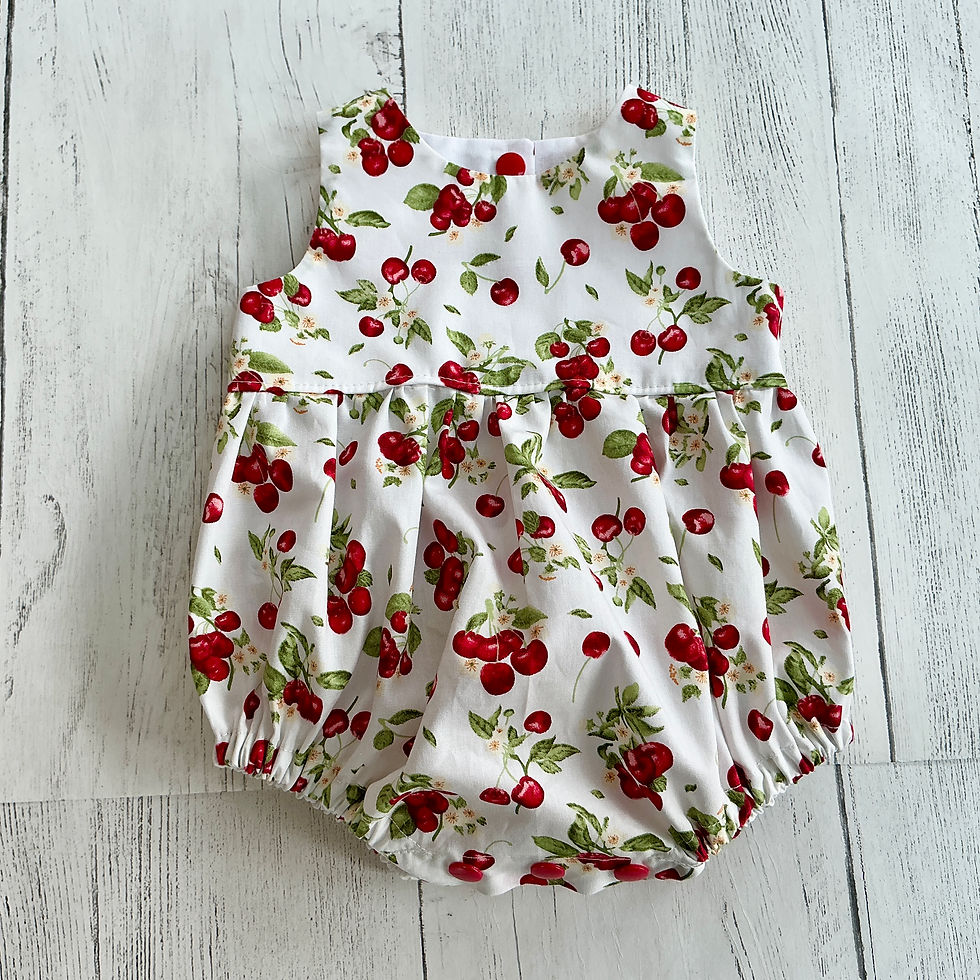 Thumbnail: Sleeveless baby romper in a cotton fabric featuring clusters of red cherries & green foliage on an off white background