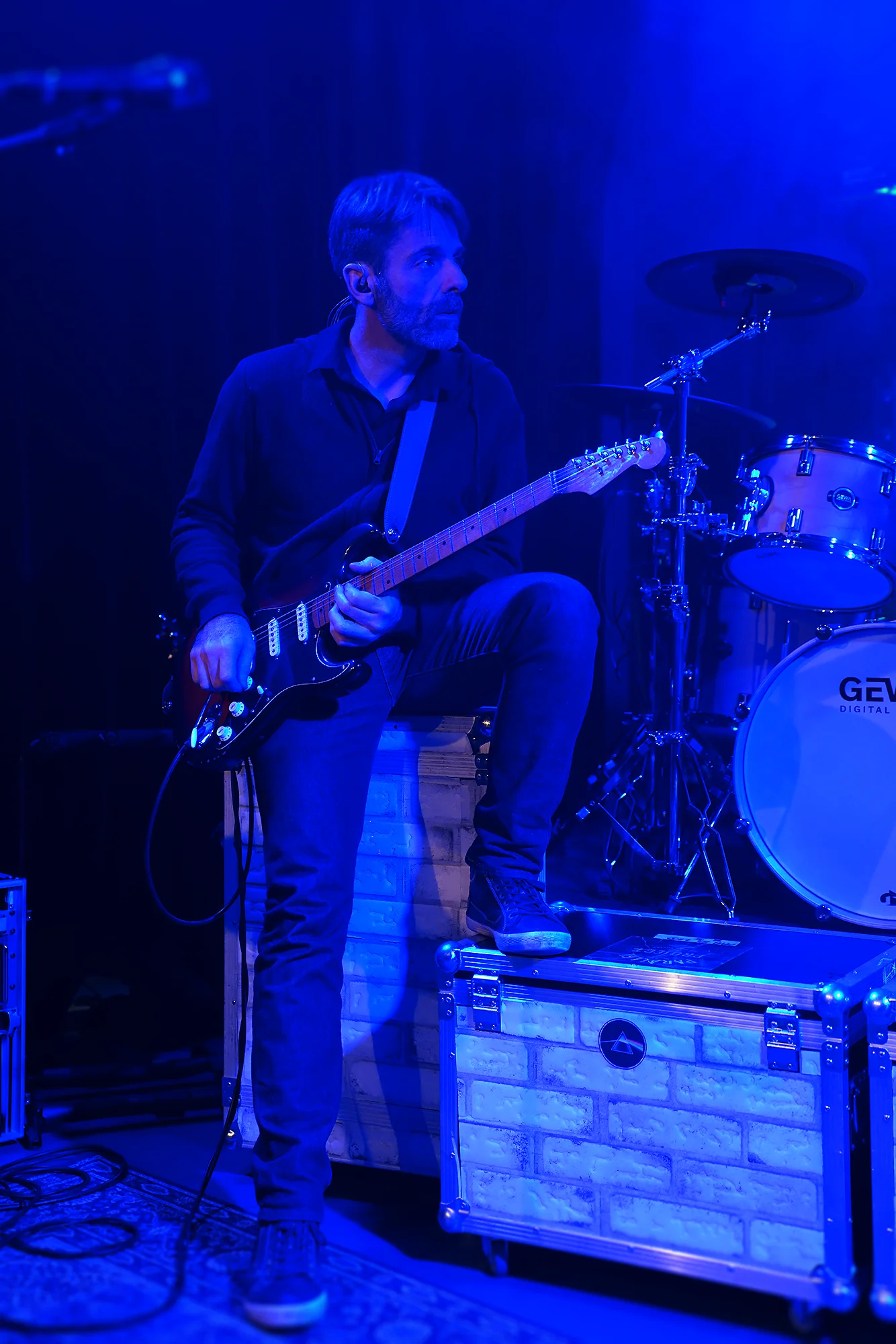 Guitariste de Parallel Project sur scène, éclairage bleu et batterie en arrière-plan lors du Tribute Fest 2025.