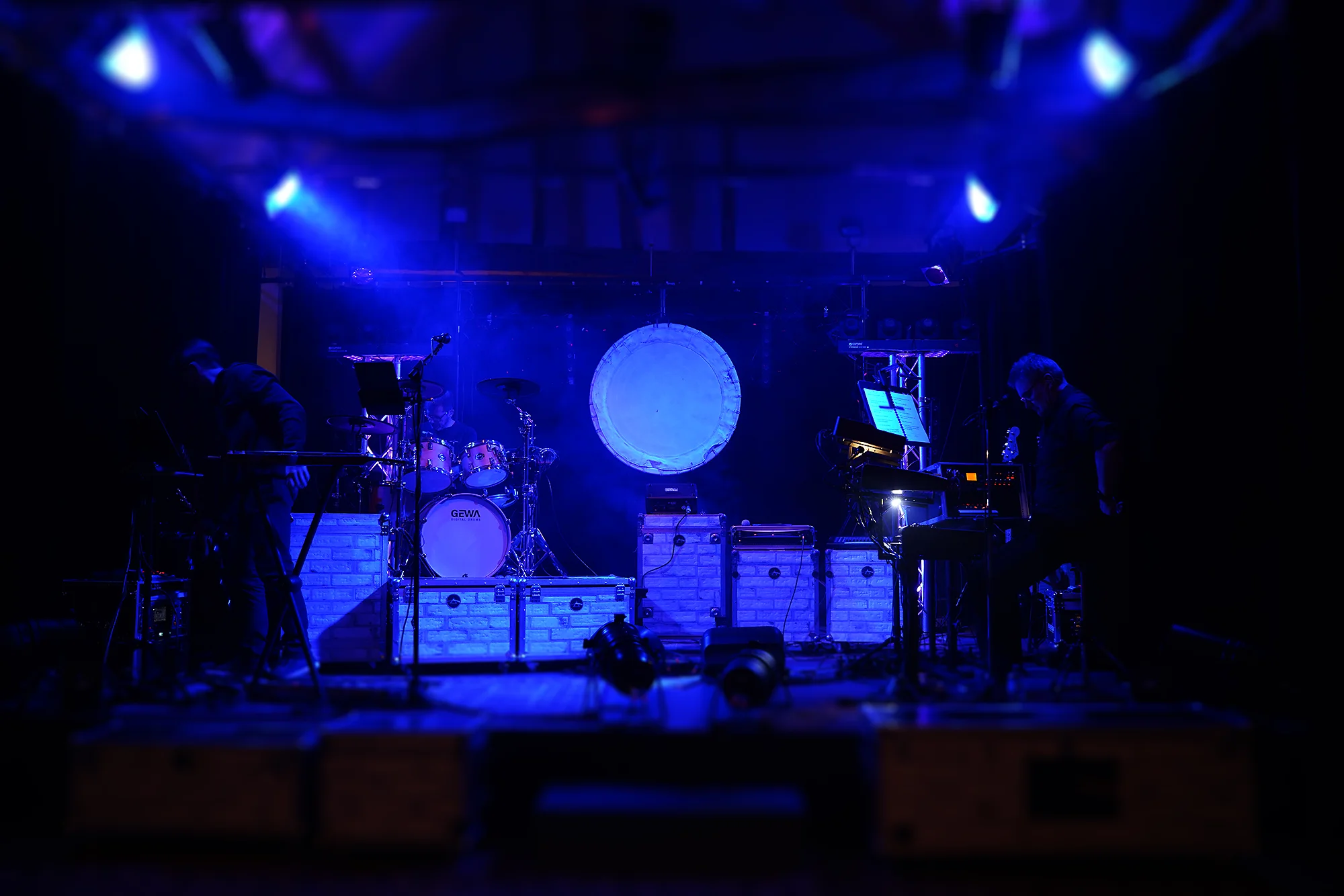 Scène de Parallel Project à la Grange aux Dîmes, éclairage bleu et grand cercle lumineux en fond de scène lors du Tribute Fest 2025.