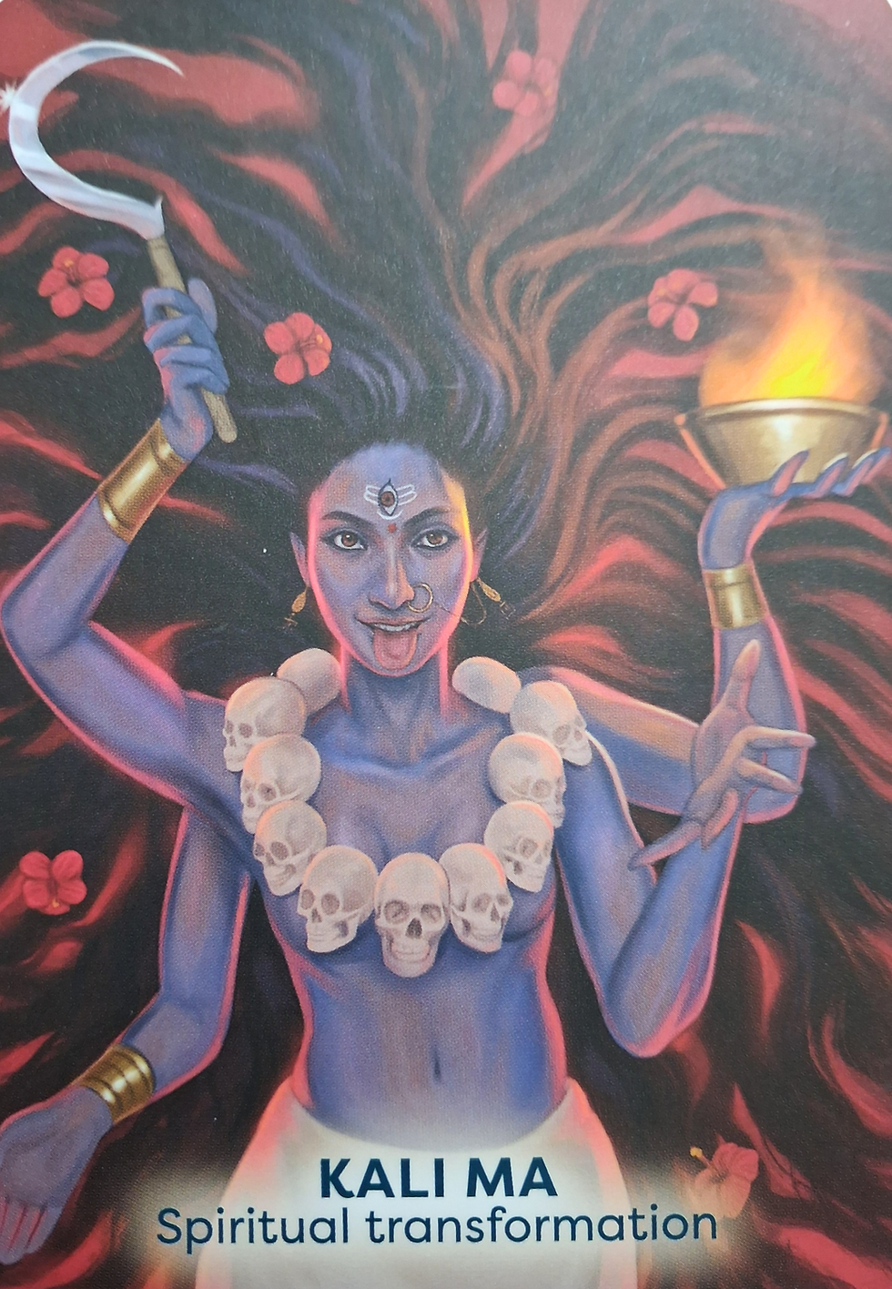 Goddess Kali oracle card depicting A blue-skinned figure with flowing hair holds a sickle and flame, adorned with a skull necklace. Text reads "Kali Ma: Spiritual Transformation."