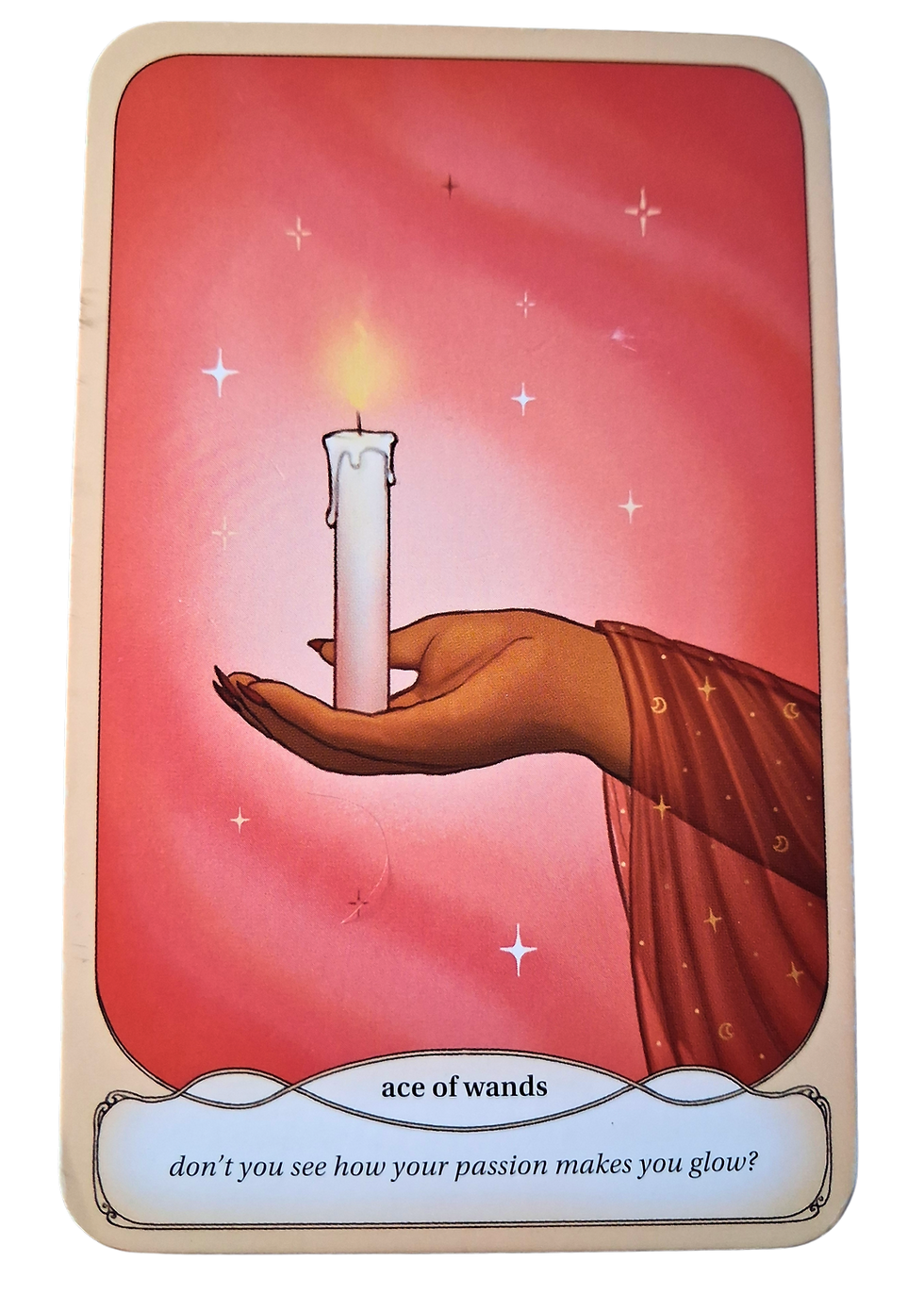 Tarot card of a hand holding a lit white candle against a pink starry background, labeled ace of wands
