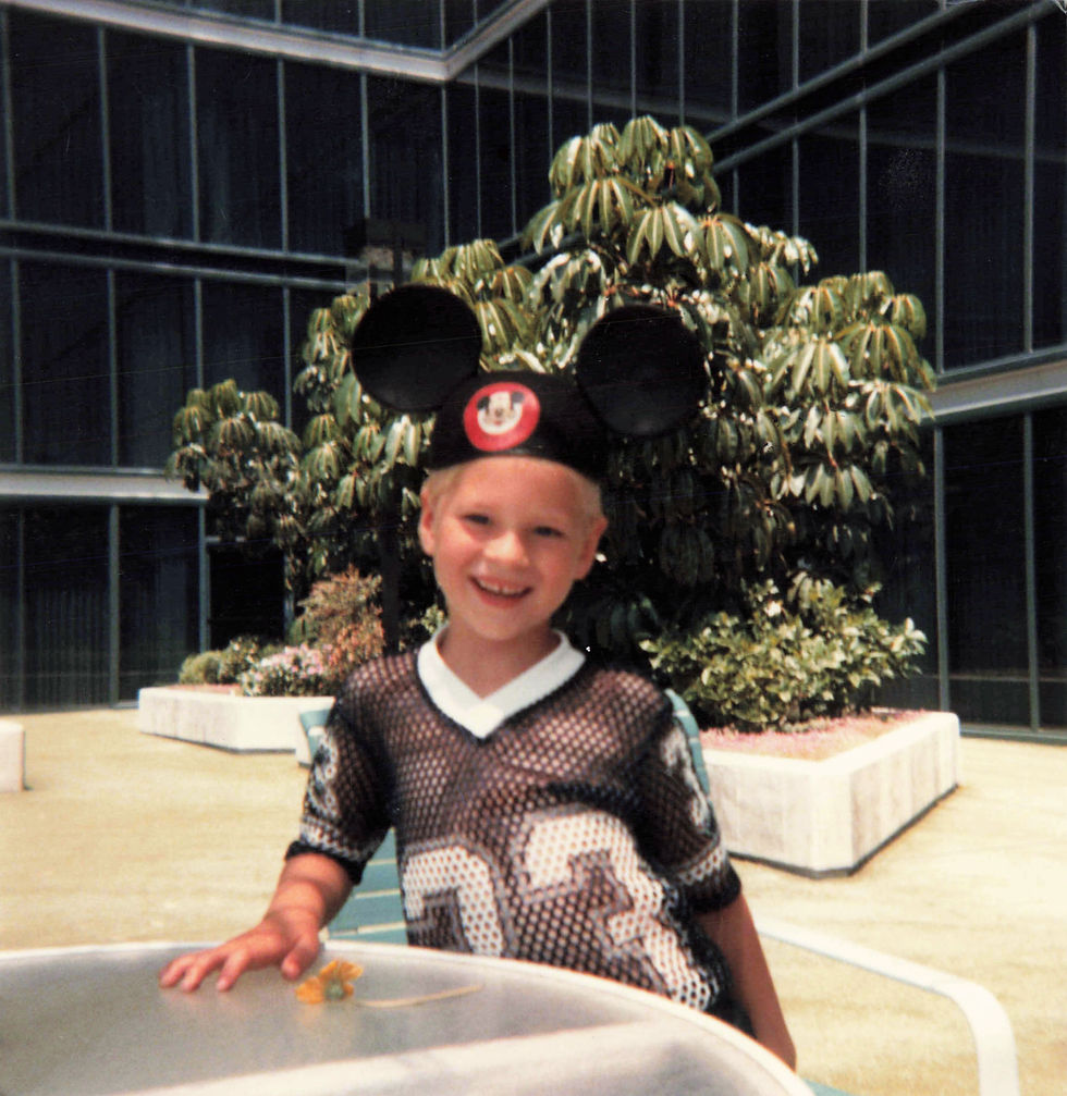 Me standing at a table wearing a black Mickey Mouse ears hat and black mesh sports shirt.