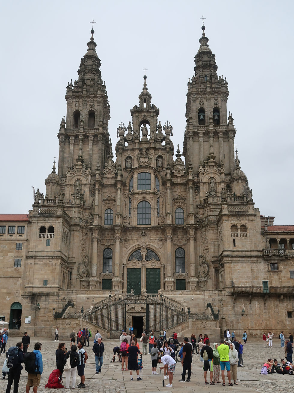 Pessoas frente à Catedral de Santiago de Compostela, Espanha, observando fachada antiga em pedra sob céu nublado. Turistas tiram fotos.