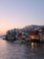 Casas à beira-mar brancas, azuis e vermelhas ao pôr do sol, com barcos parados em águas calmas, no bairro Little Venice, Míconos, Grécia