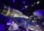 Space exhibit with a large suspended spacecraft and capsules. Purple lighting creates a futuristic mood. "Lockheed Martin" and "Boeing" visible. Kennedy Space Center Visitor Complex