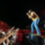 Singer in jeans and cap performs on stage at night, with excited crowd reaching up. Red lights and palm trees create a vibrant scene. Luke Bryan returns to Orlando's Kia Center on June 13 for the Country Song Came On Tour