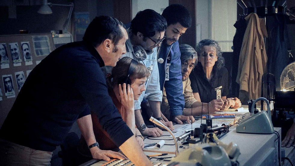 SEPTEMBER 5 featuring an Impressive Ensemble Cast. People gathered around a desk in a dimly lit control room, focusing intently. Miscellaneous equipment and photographs on the wall.