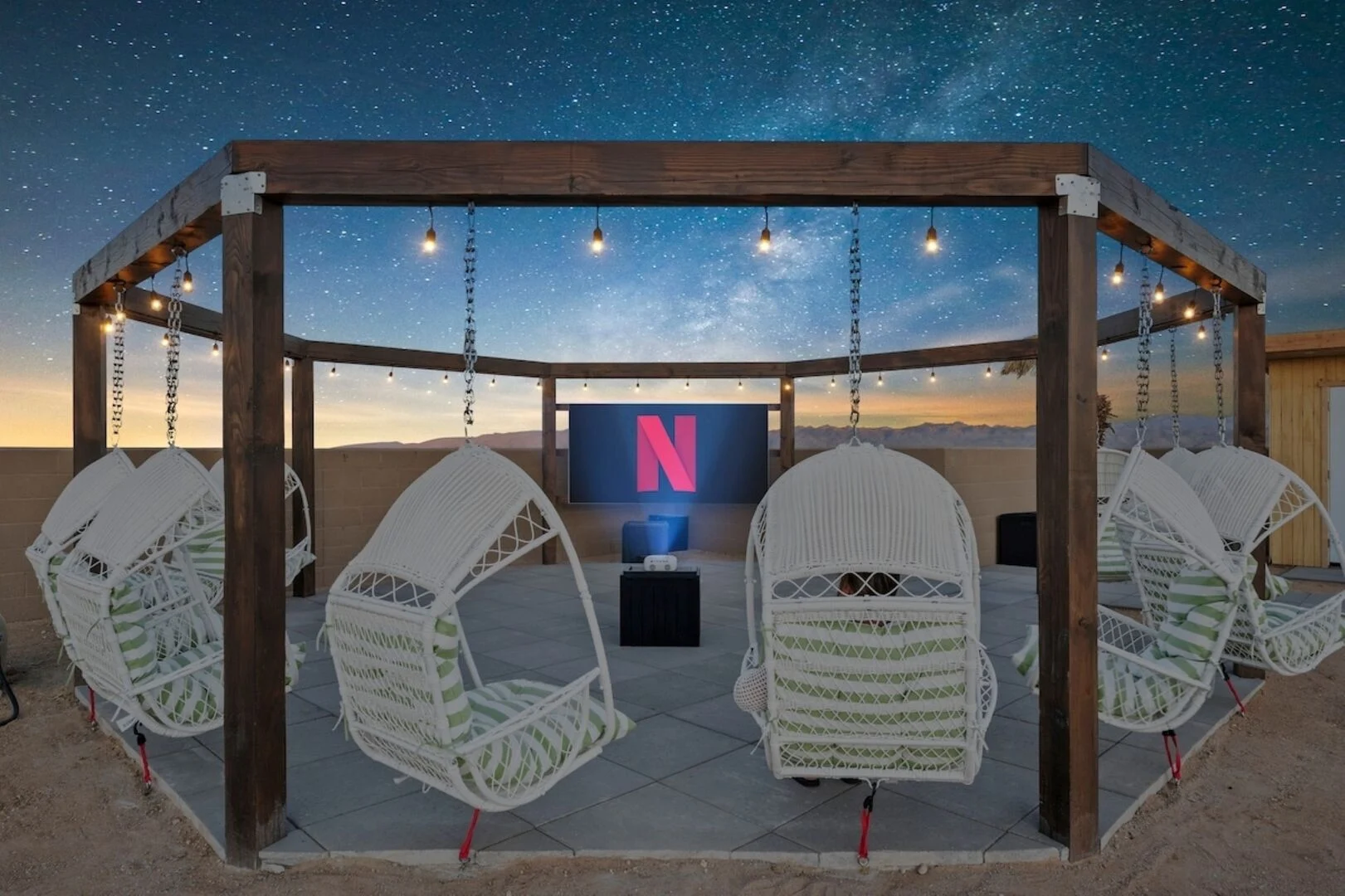 Netflix projecting on to a screen under the night sky with swinging chairs around the screen 