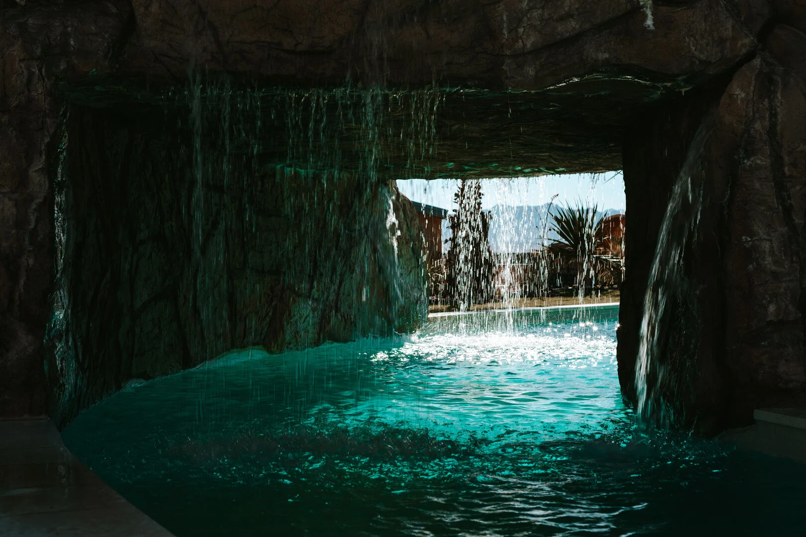 a grotto with a waterfall in the lazy river with water falling form above 
