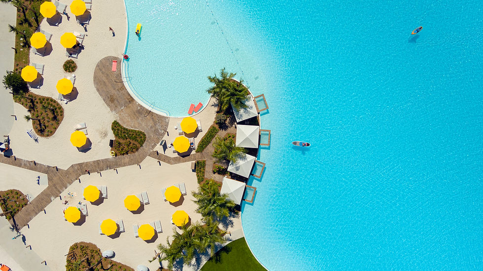 aerial view looking down at the yellow sun umbrellas and lounge chairs scattered on the white sand beaches next to the massive blue evermore bay pool with cabins and kayaks in the water