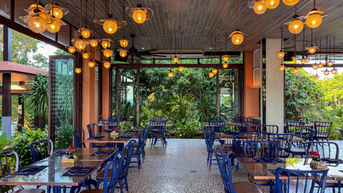 open air dining restaurant with orange hanging lights and blue chairs surrounded by lush green jungle vegetation outside the open doors and windows
