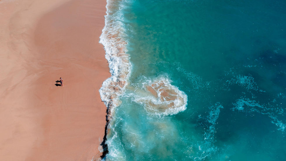 Aerial view looking down as a man and woman stand by the crashing waves on the beach